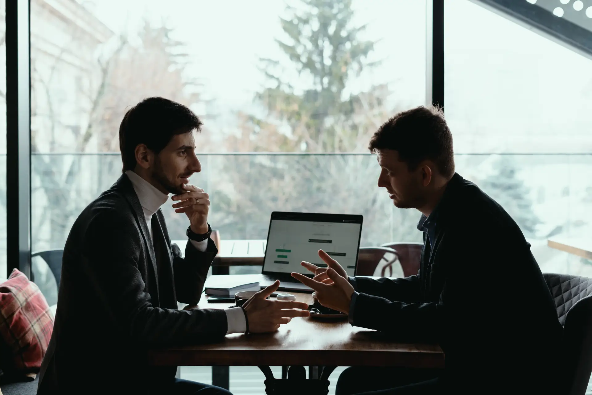 Two businessmen having a discussion with a laptop open between them.