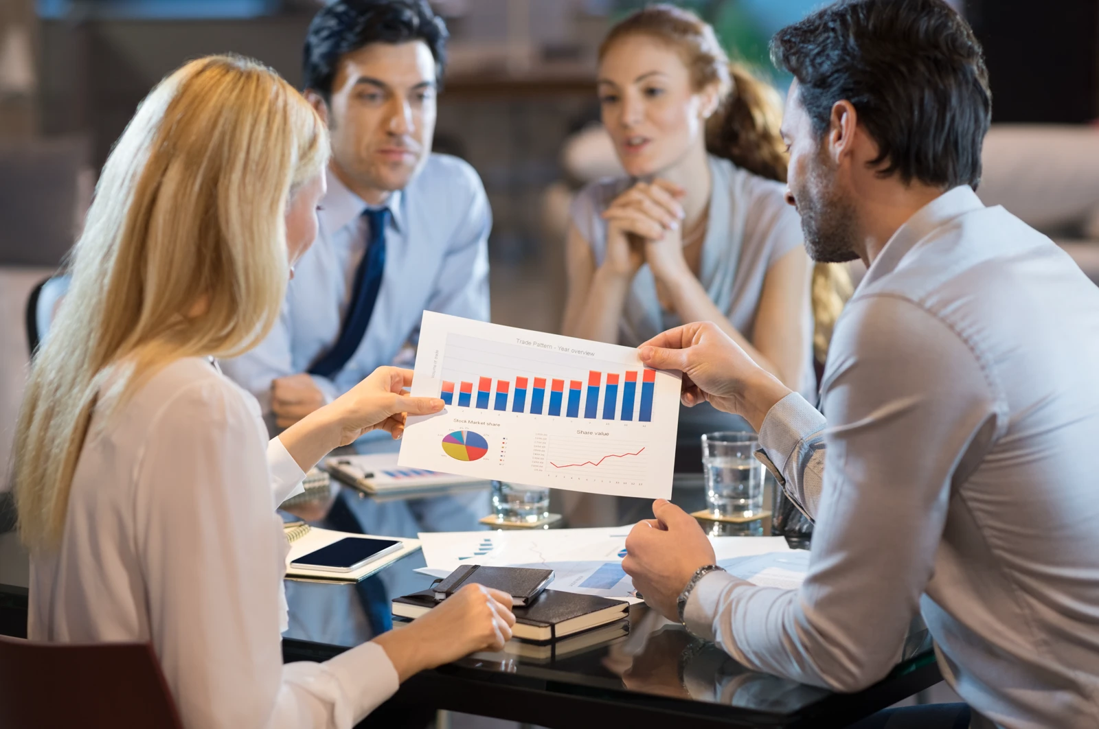 A group of four business professionals sitting around a glass conference table