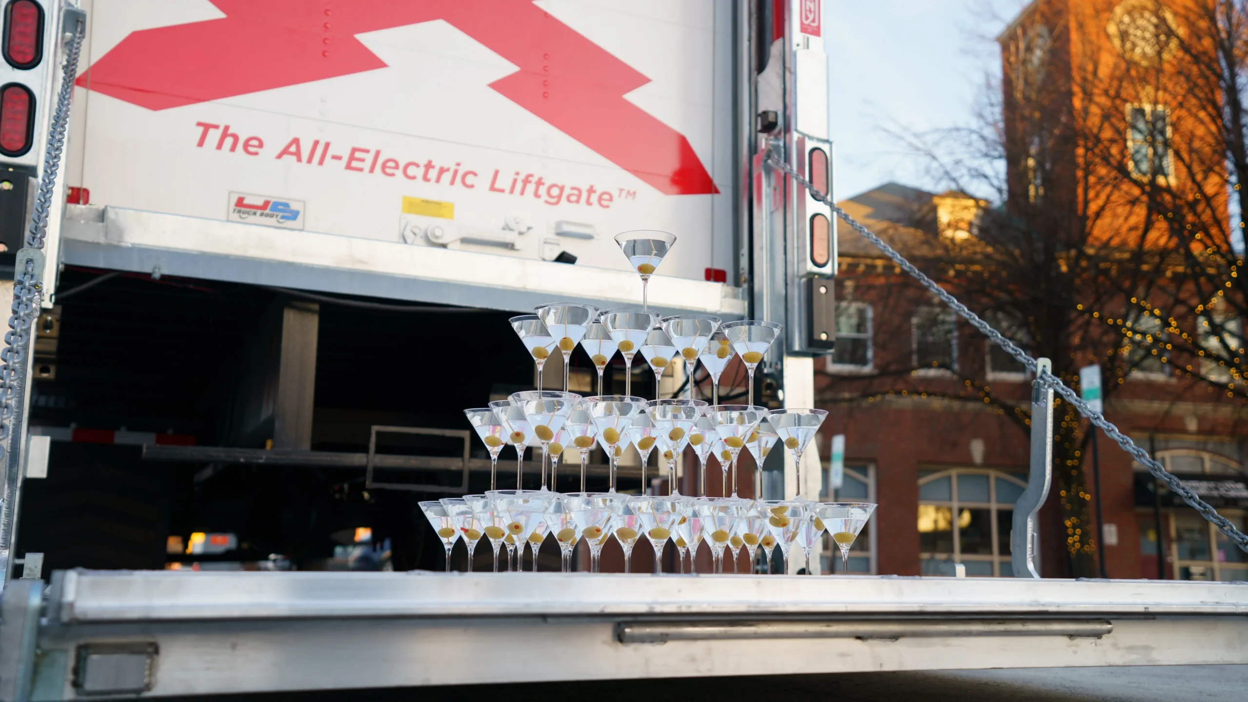 Martini glass tower stunt demonstrating stability on a truck liftgate labeled The All-Electric Liftgate
