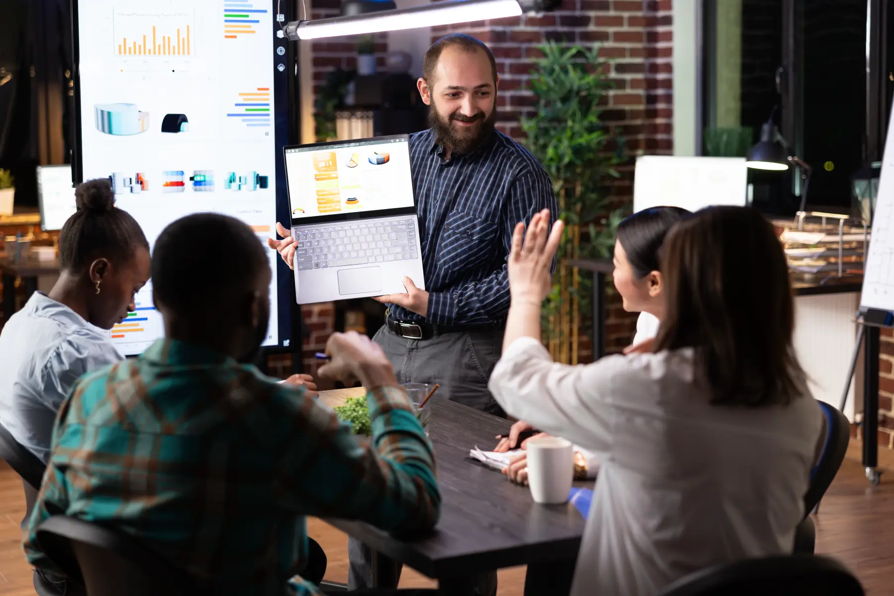 A team lead presents data on a laptop to a group of colleagues